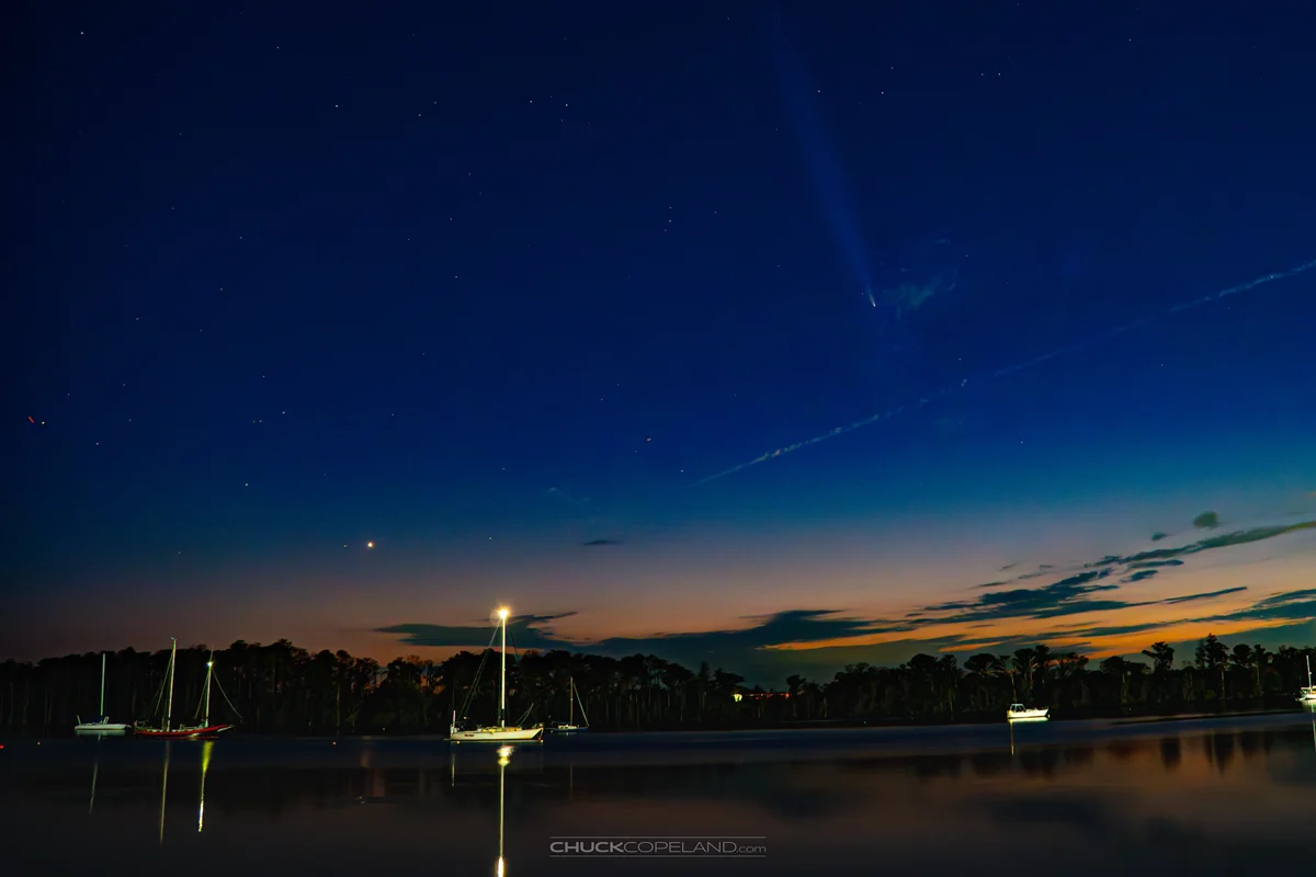 A comet and stars above sailboats at twilight